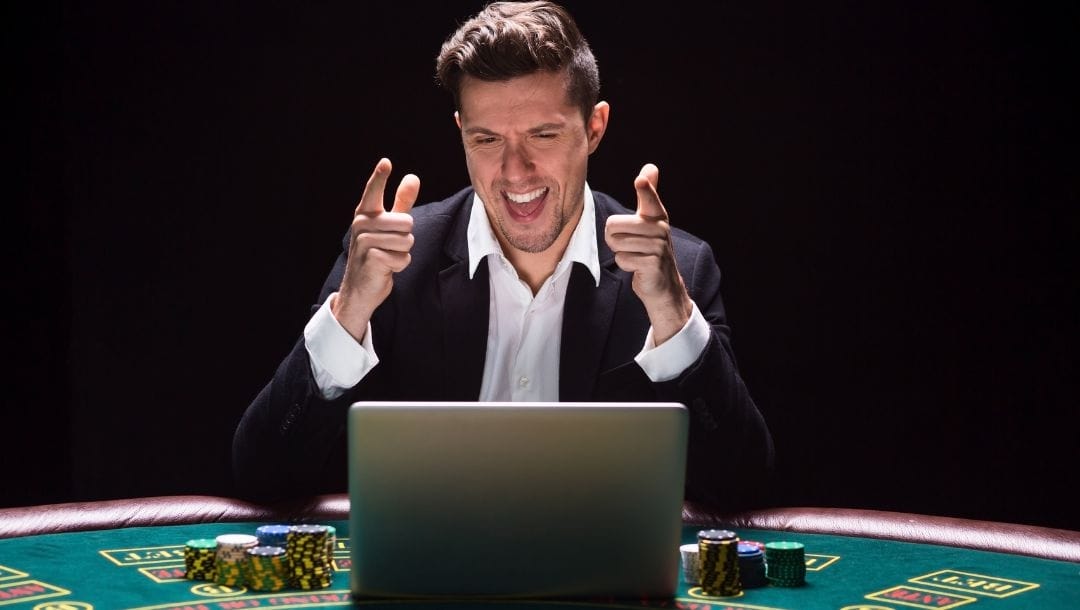 a man celebrating in front of a laptop on a casino poker table with poker chips stacked next to it