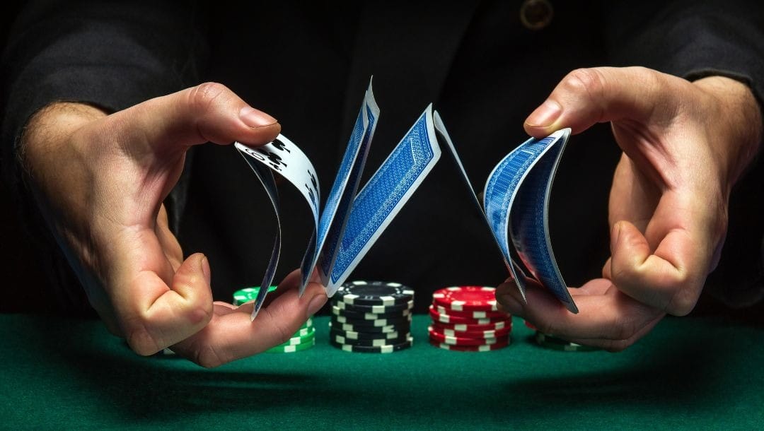 a dealer shuffling cards above a green felt poker table with stacks of poker chips on it
