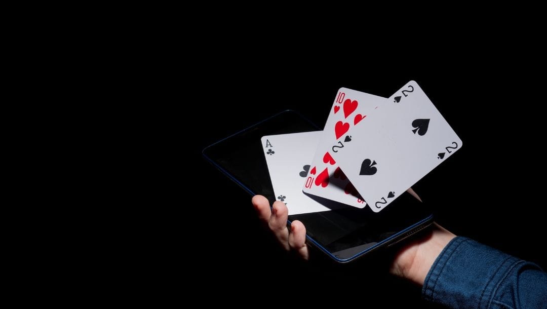a person’s hand holding out a digital tablet with playing cards flying off of it