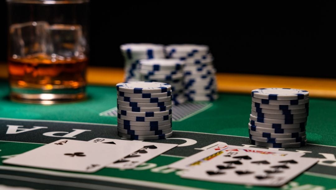 poker chips and playing cards on a blackjack table next to a glass of whiskey