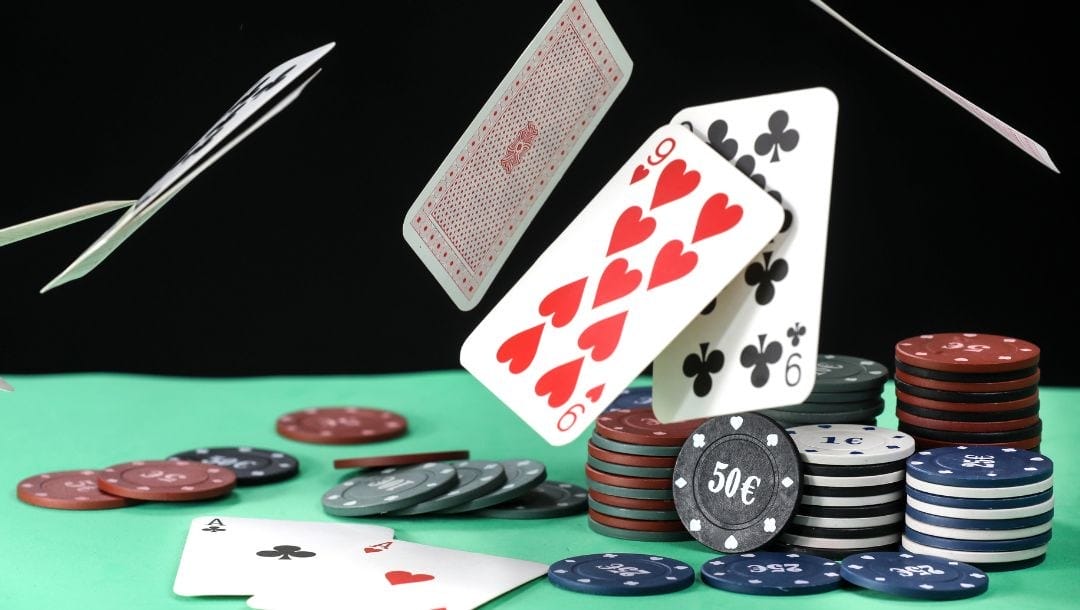 stacked poker chips and playing cards flying around on a green felt poker table