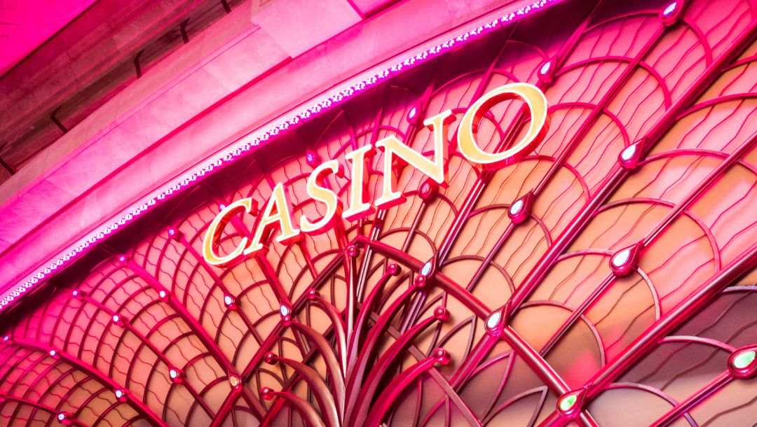 a neon light sign that reads “CASINO” on a pink lit casino building