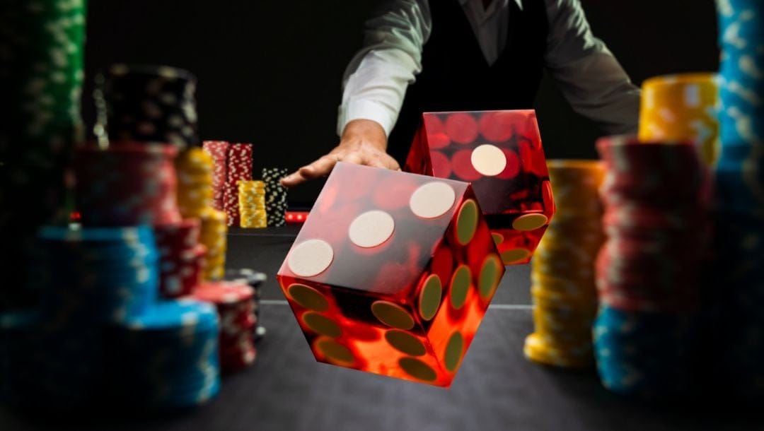 a man throwing a pair of six sided dice onto a craps table in between stacks of poker chips in a casino