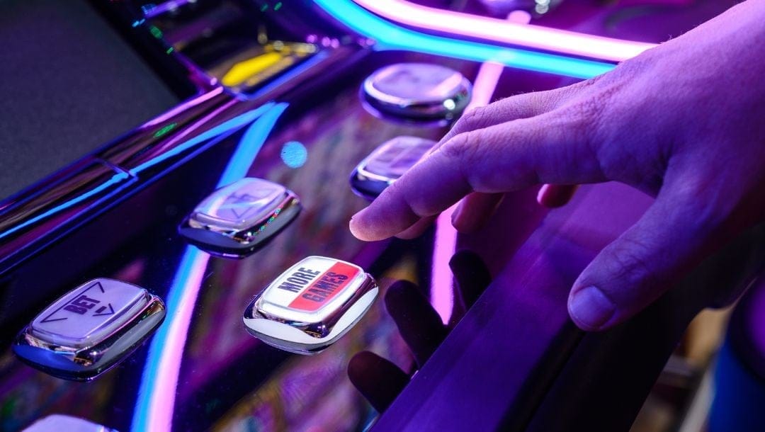 a close up of a person’s hand about to push the “More Games” button on a slot machine in a casino
