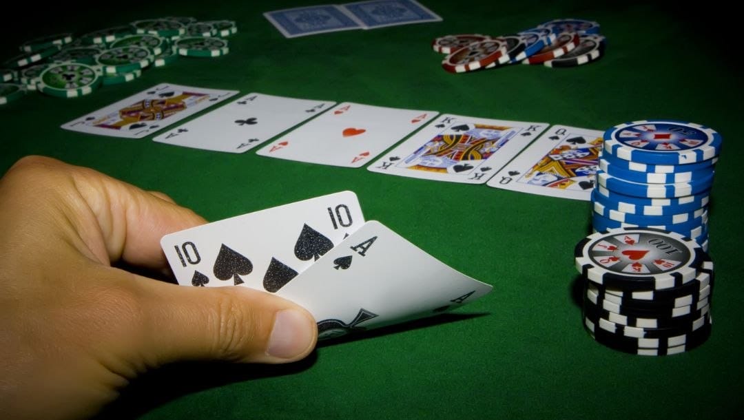 a man checking his hole cards, a ten and ace of spades, post flop during a game of poker on a green felt poker surface stacked with poker chips