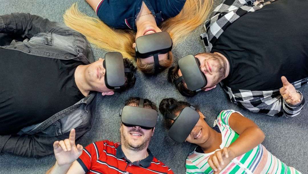 five people are wearing virtual reality headsets laying in a circle on the ground with their heads together looking up and pointing