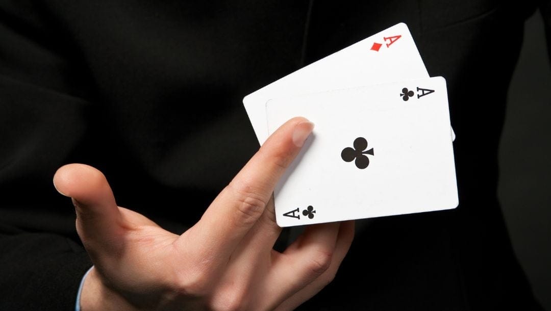 a person is holding a pair of ace playing cards, a diamond and a club, in between their middle and index fingers