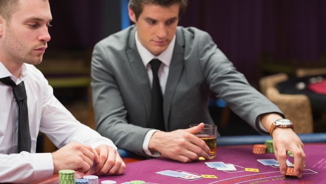 two men playing at a blackjack table in a casino