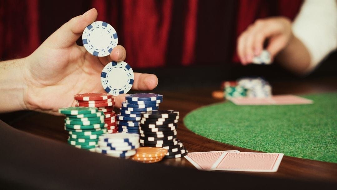 a close up of a person picking up poker chips from the stacks on a poker table with a player opposite them