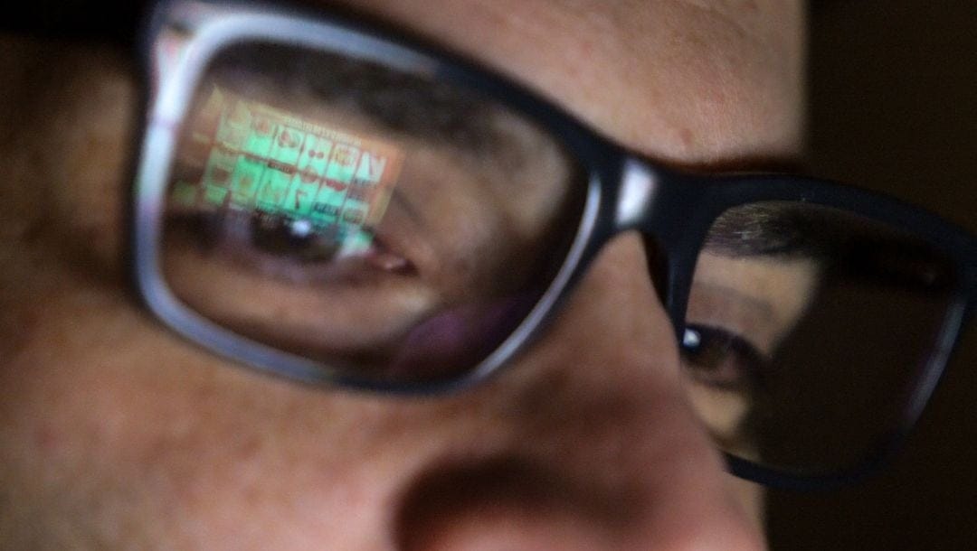 close up of a man wearing glasses that are reflecting a laptop screen that displays online slots