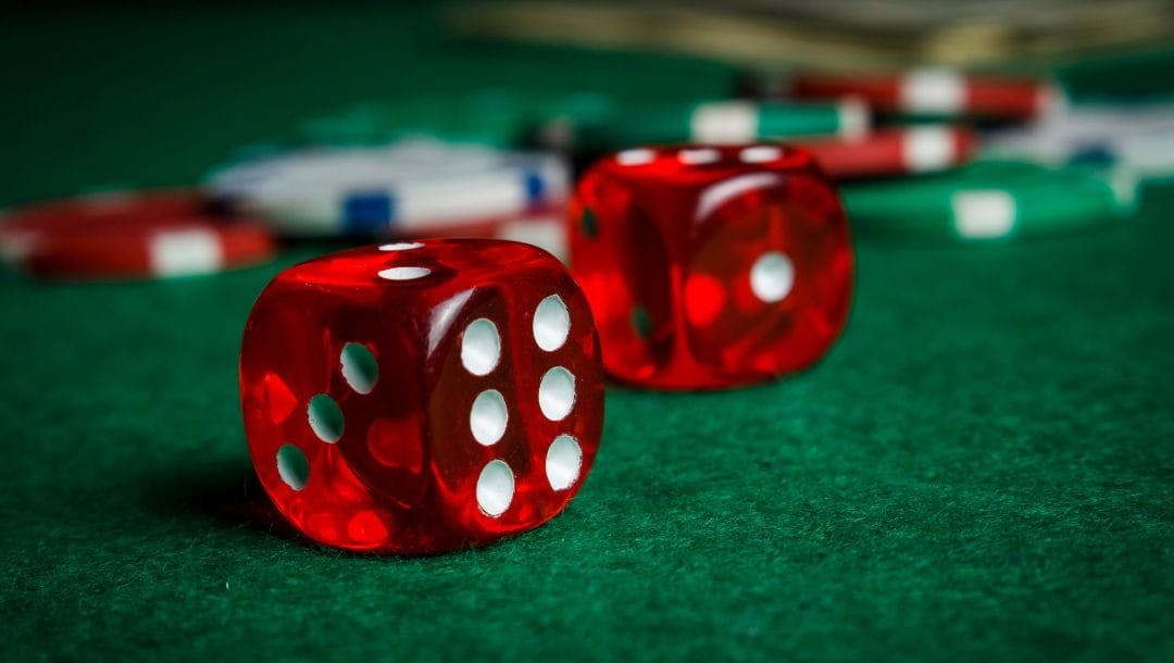 a pair of red six-sided dice on a green felt poker table with poker chips blurred in the background