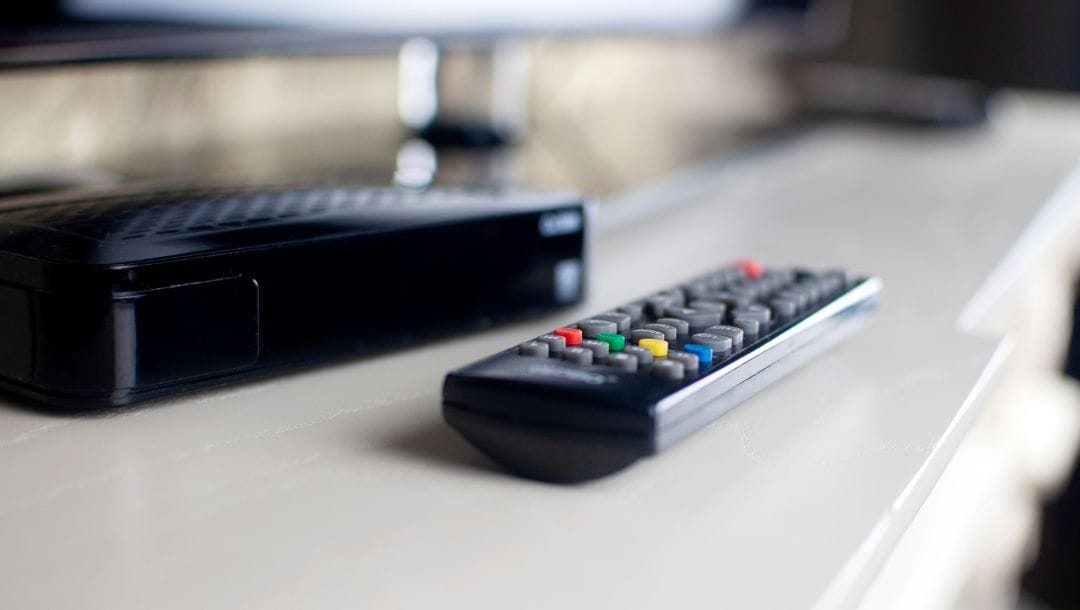 a remote control in front of a TV decoder on a white TV cabinet