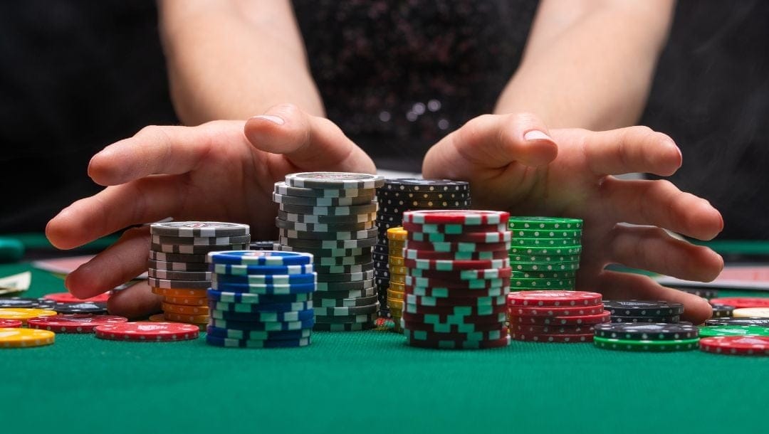 a woman’s hands pushing stacks of poker chips forward on a green felt poker table