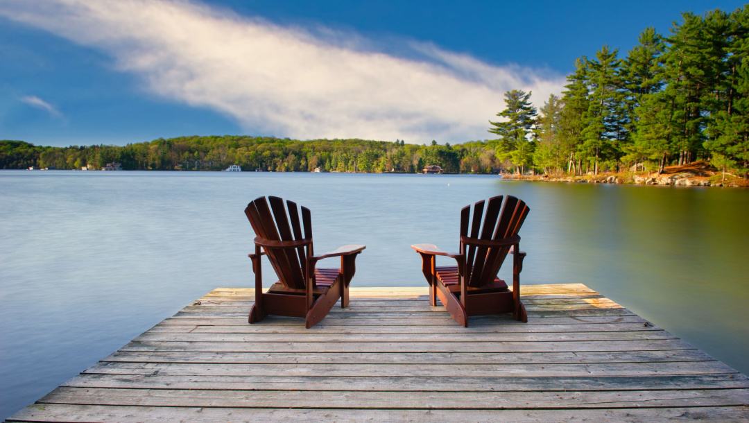 Two wooden chairs out on a deck looking over a lake.