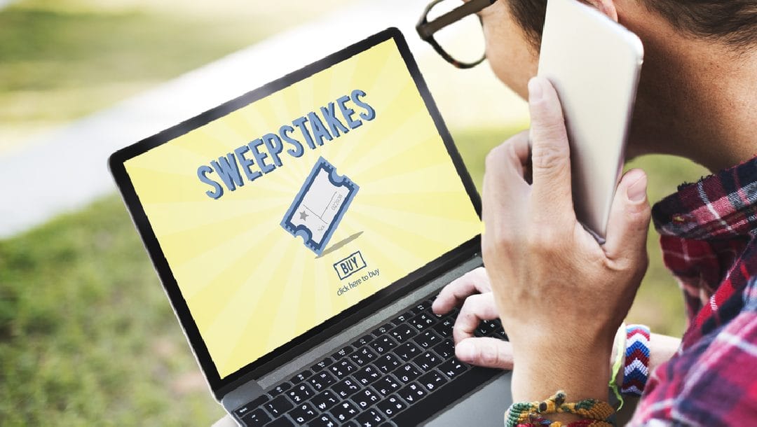 A person looks at sweepstakes tickets on a laptop while talking on a cell phone.