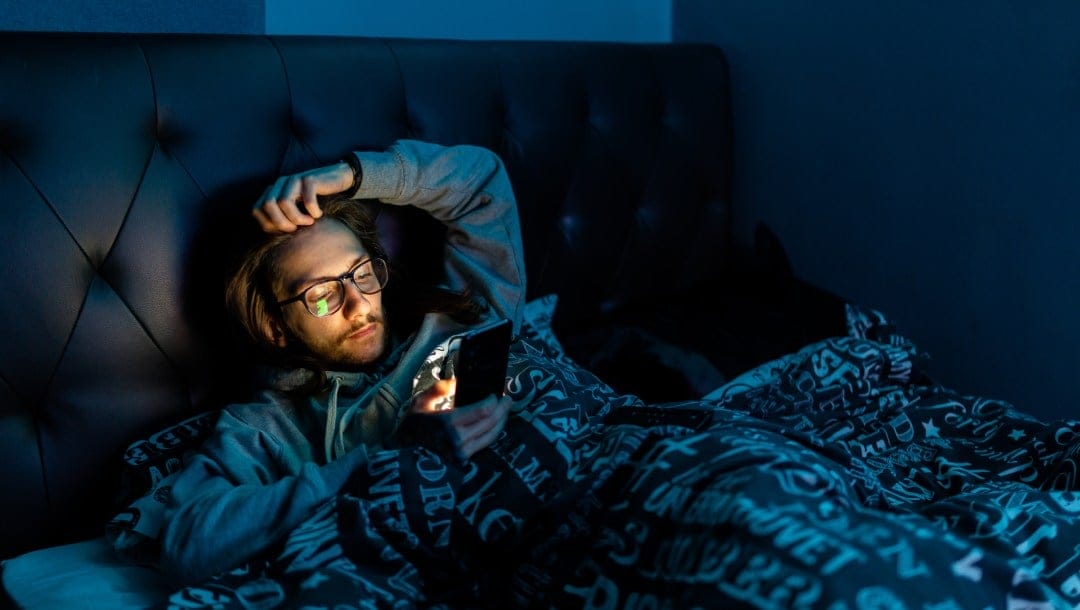 A man on a bed with a smartphone in his hand.