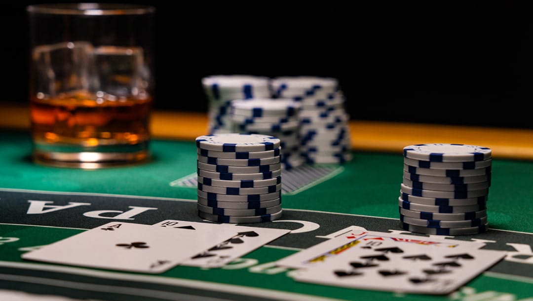 White and blue casino chips and playing cards on a green, black and white blackjack table. The background is black.