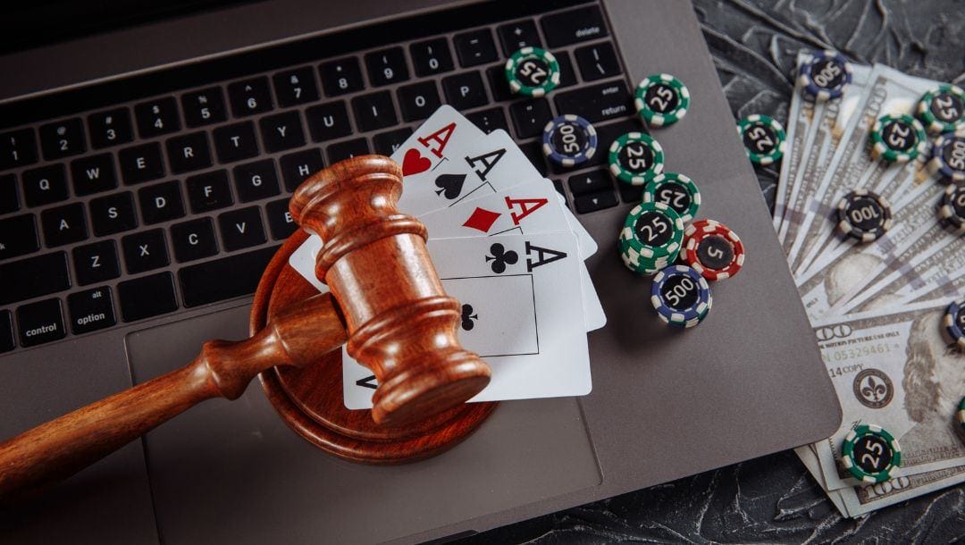top view of four of a kind ace playing cards, poker chips and a gavel on a laptop keyboard next to hundred dollar money bills and more poker chips