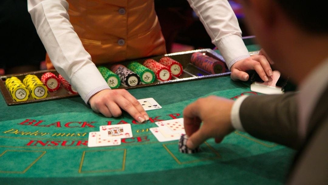 a man placing poker chips down on a blackjack table as the dealer points at the playing cards on the table