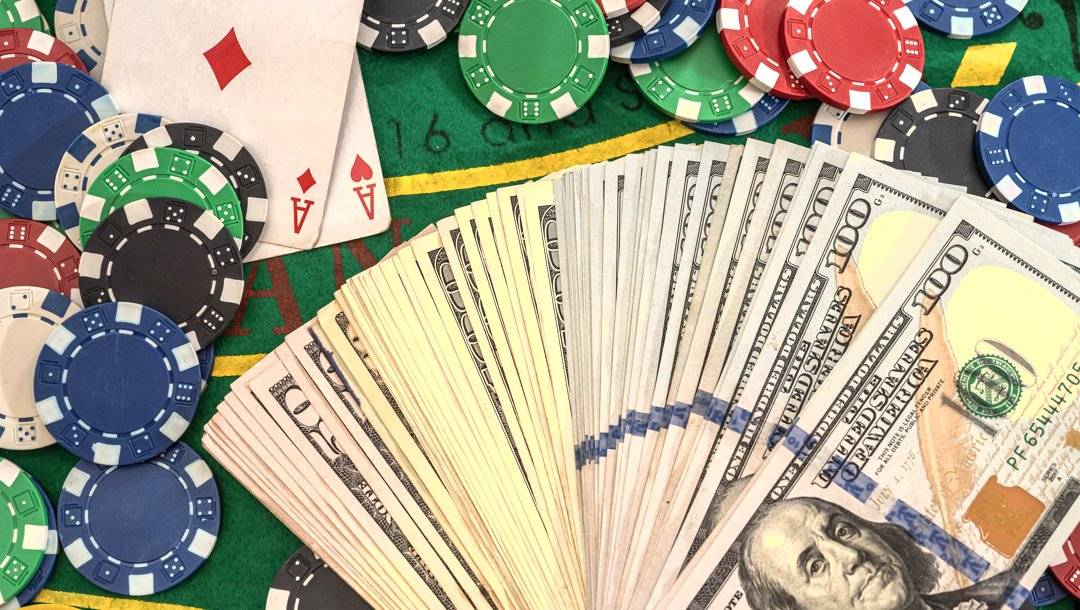 Two aces next to stacks of poker chips and a pile of dollar bills laid out in a fan shape.