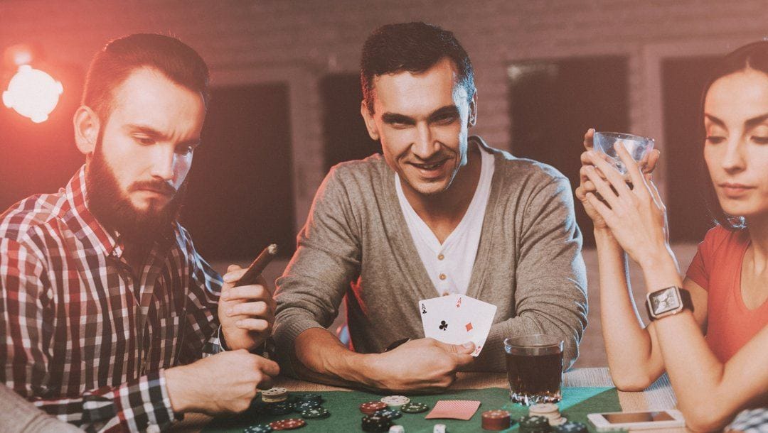 A man playing poker with his friend reveals his hole cards. His hole cards are a pair of aces.