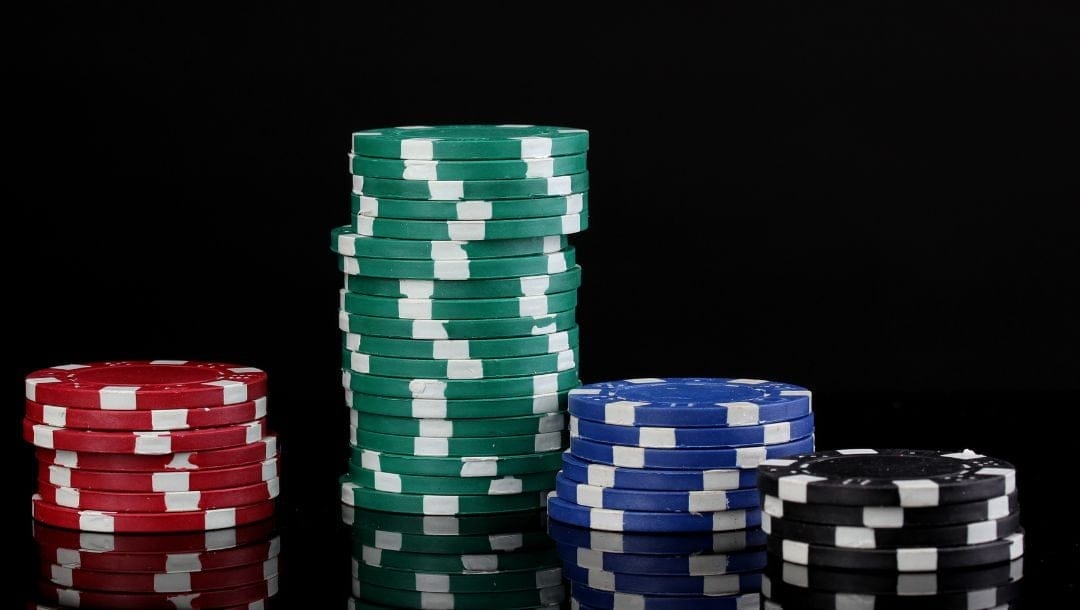 Stacks of casino chips organized by color - black, blue, red, and green - against a black background.
