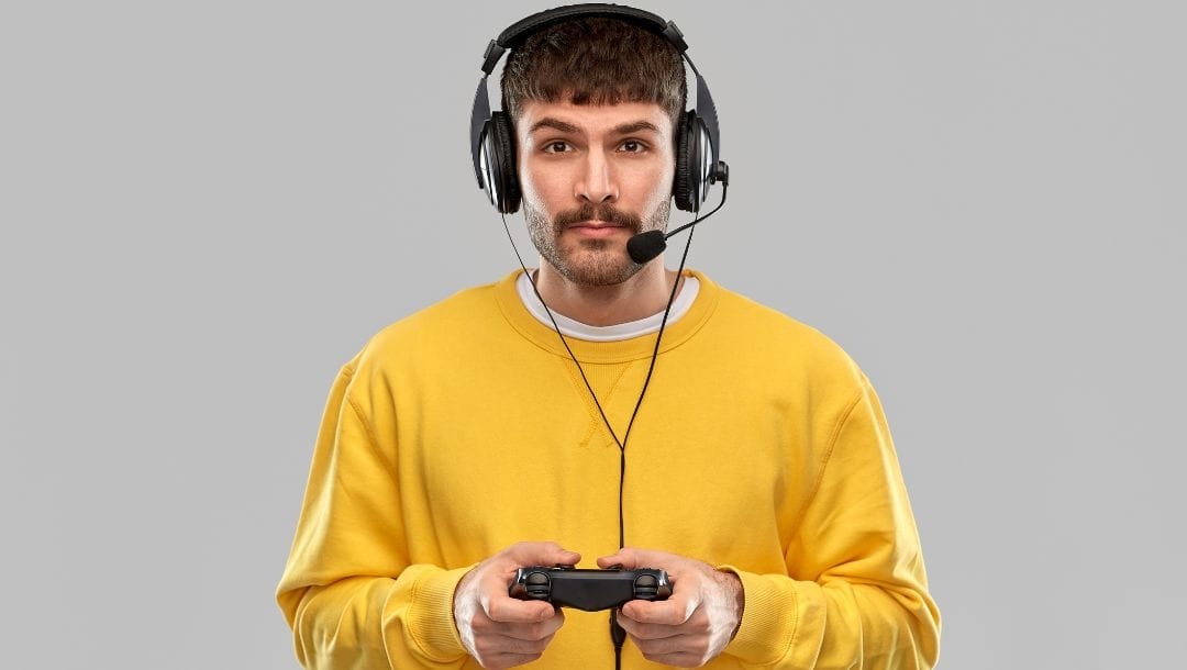 A man in a yellow sweater, holding a console remote and wearing a gaming headset with a microphone.