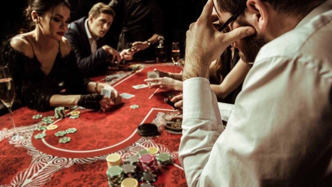 People sitting around a red poker table, playing poker.