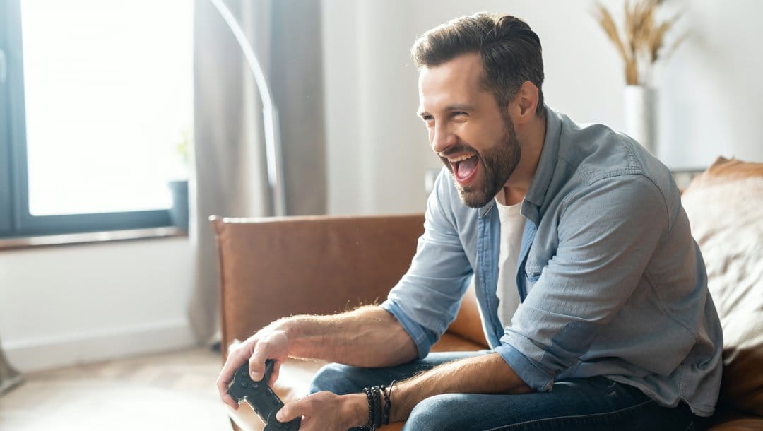 A man sitting on a couch smiles while playing video games.