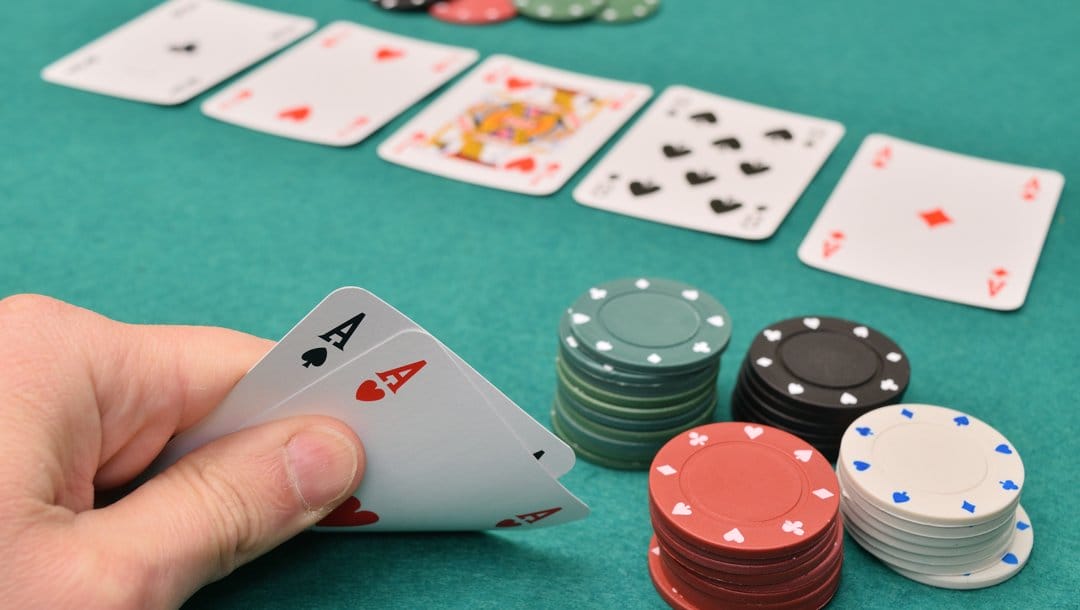 A poker player takes a look at their hole cards. There are two aces next to the player’s stacks of poker chips. There are also five community cards already on the table.