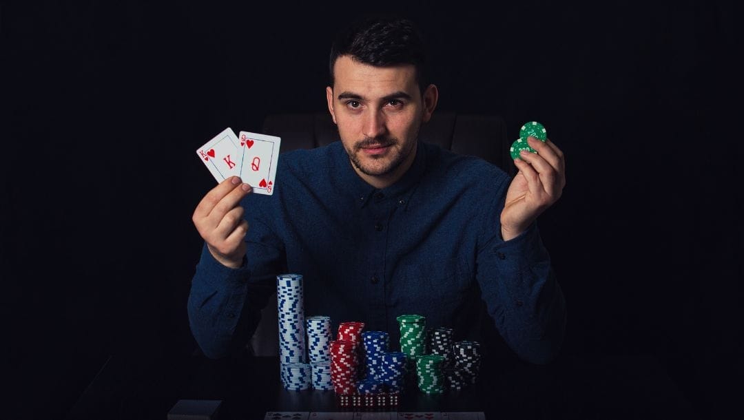 a man holding two playing cards and two green poker chips is sitting at a table that has stacks of poker chips on it