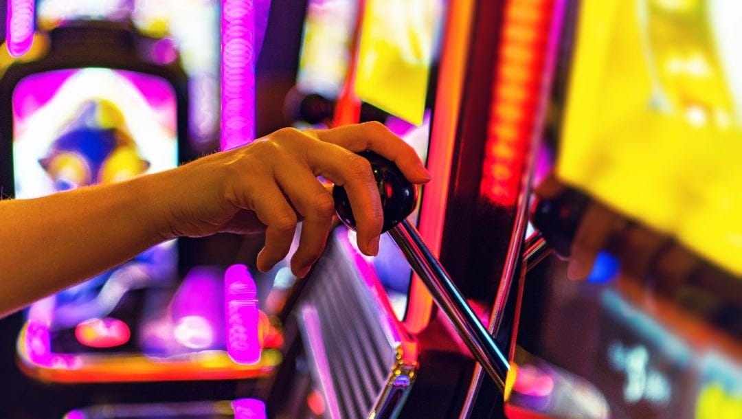 close up of a person’s hand pulling the slot machine arm down at a casino