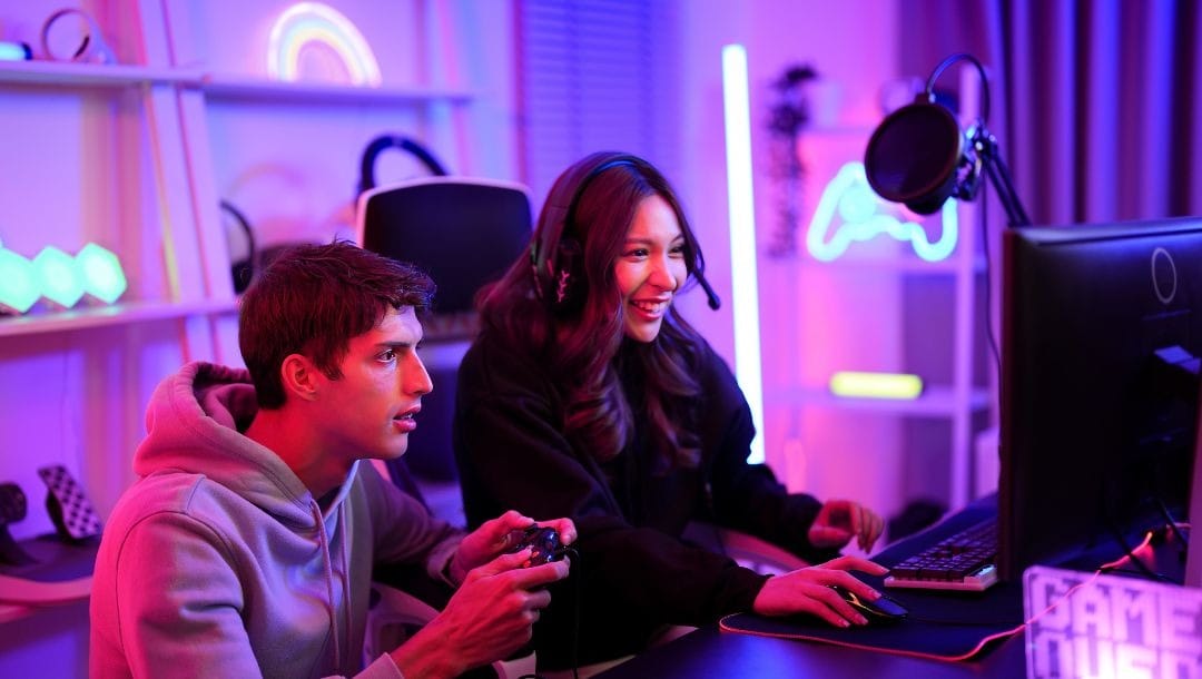 a young couple are playing video games together in a gaming room lit with pink ambient lighting