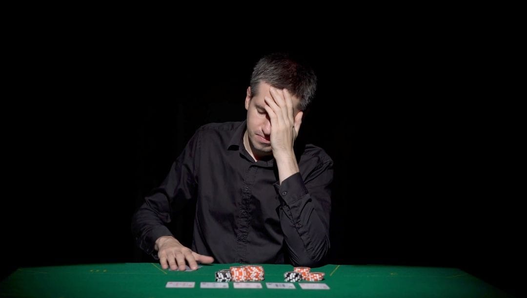 a man has his hand to his forehead in despair as he sits at a poker table