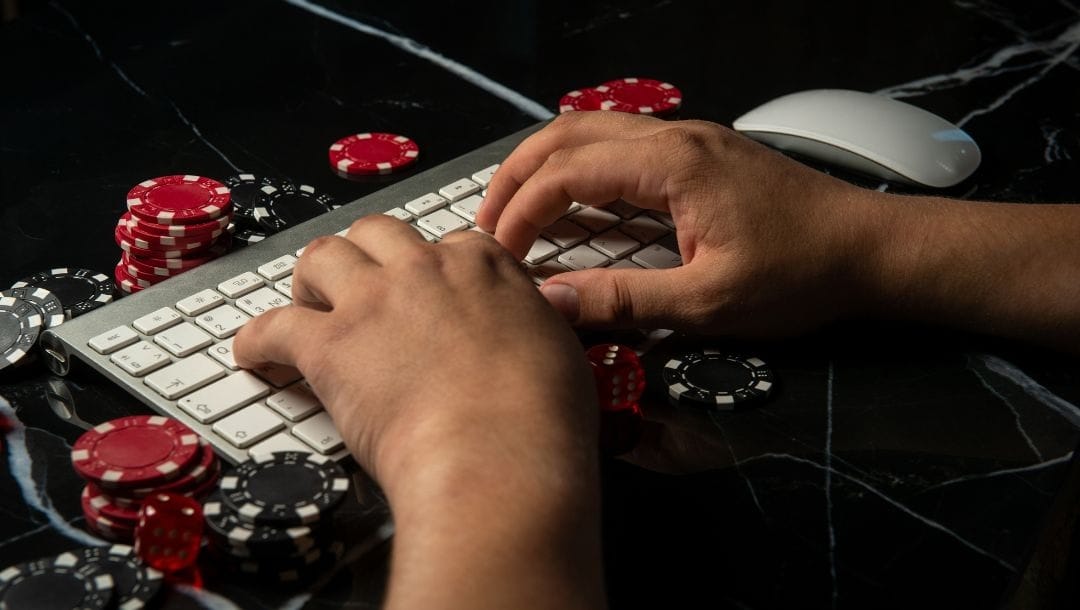 a man typing on a computer keyboard surrounded by black and red poker chips on a marble surface