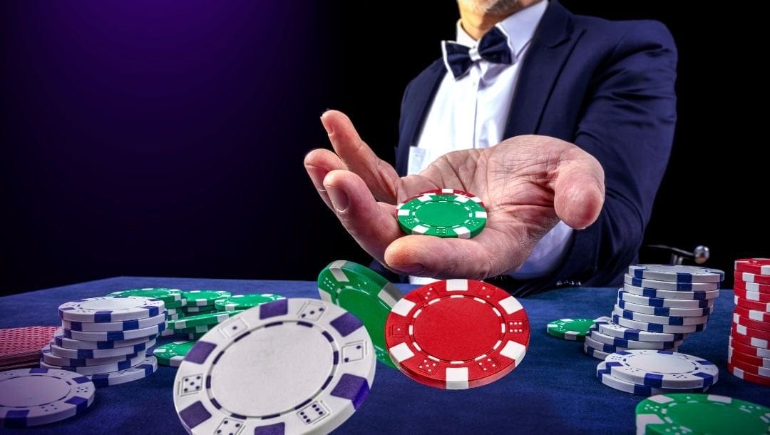 a man in a suit and bowtie holds his hand out with poker chips in it above a blue felt poker table with other poker chips on it