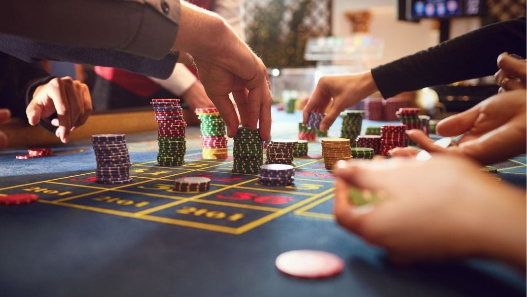 many people’s hands reaching to place bets on a roulette table in a casino