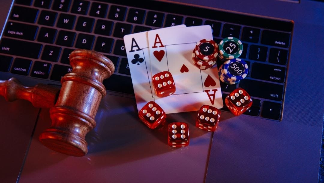 five red six-sided dice, a pair of ace playing cards, poker chips and a gavel on a laptop keyboard