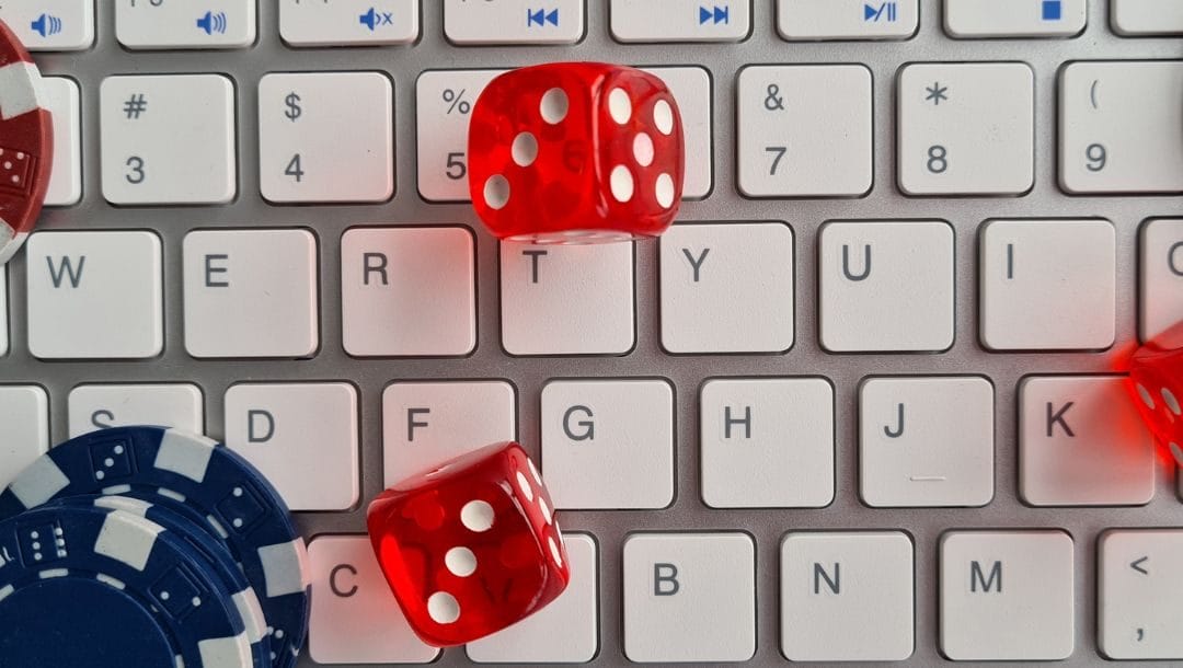 a top view of three red six-sided dice and poker chips on a white computer keyboard