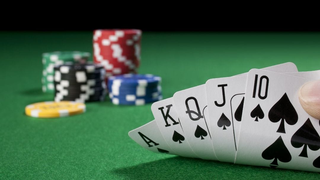 a royal flush of spades on a green felt poker table with poker chips on it in the blurred background