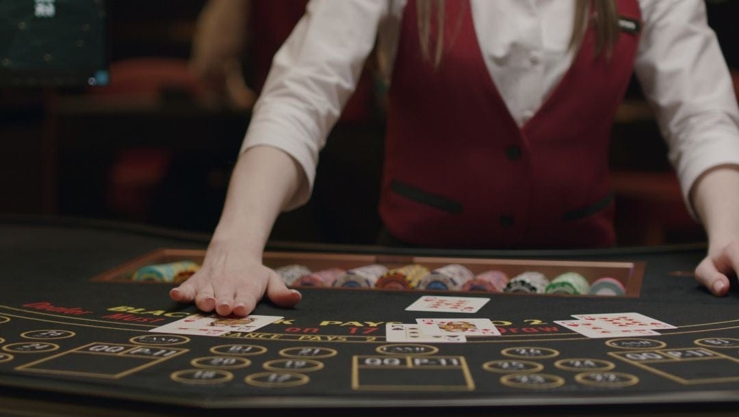 a blackjack dealer swiping the blackjack table with playing cards on it in a casino