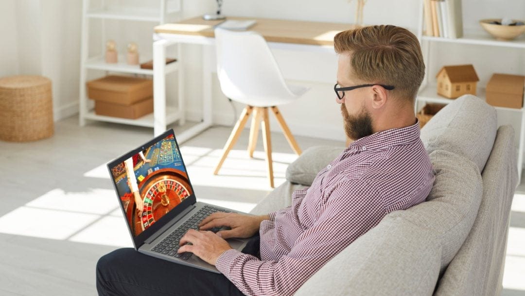 A man sitting on a couch playing online roulette on his laptop.