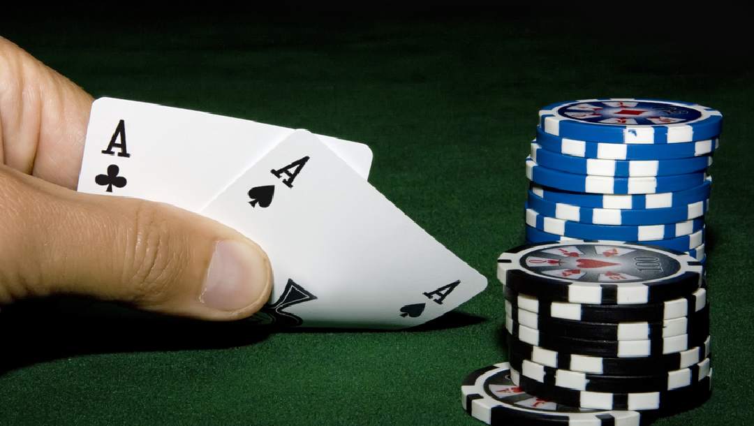A player looks at an ace-pair next to chips on a poker table.