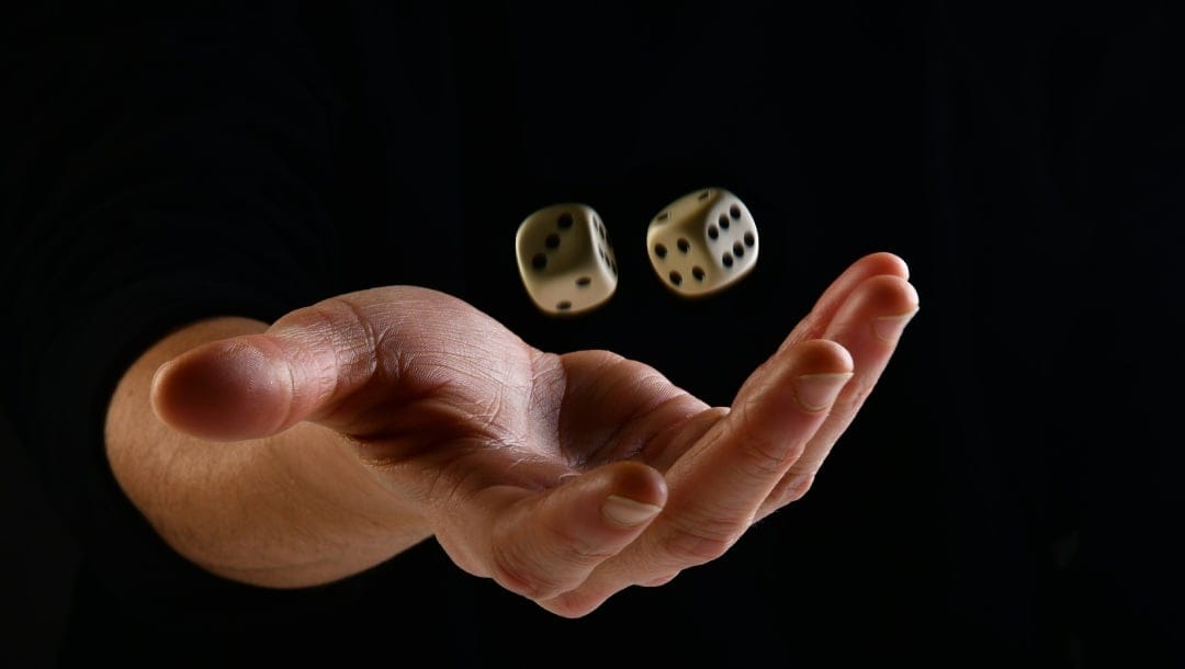 A hand throwing dice in the air against a black backdrop.