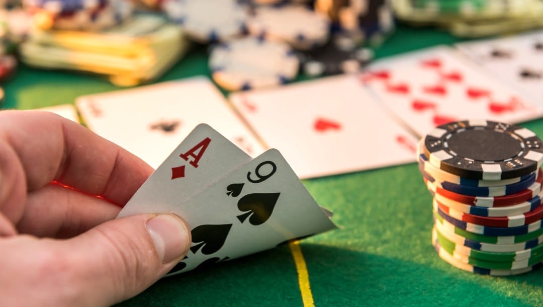 A hand holding poker cards on a poker table.