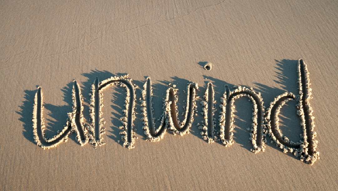 The word “unwind” written in beach sand