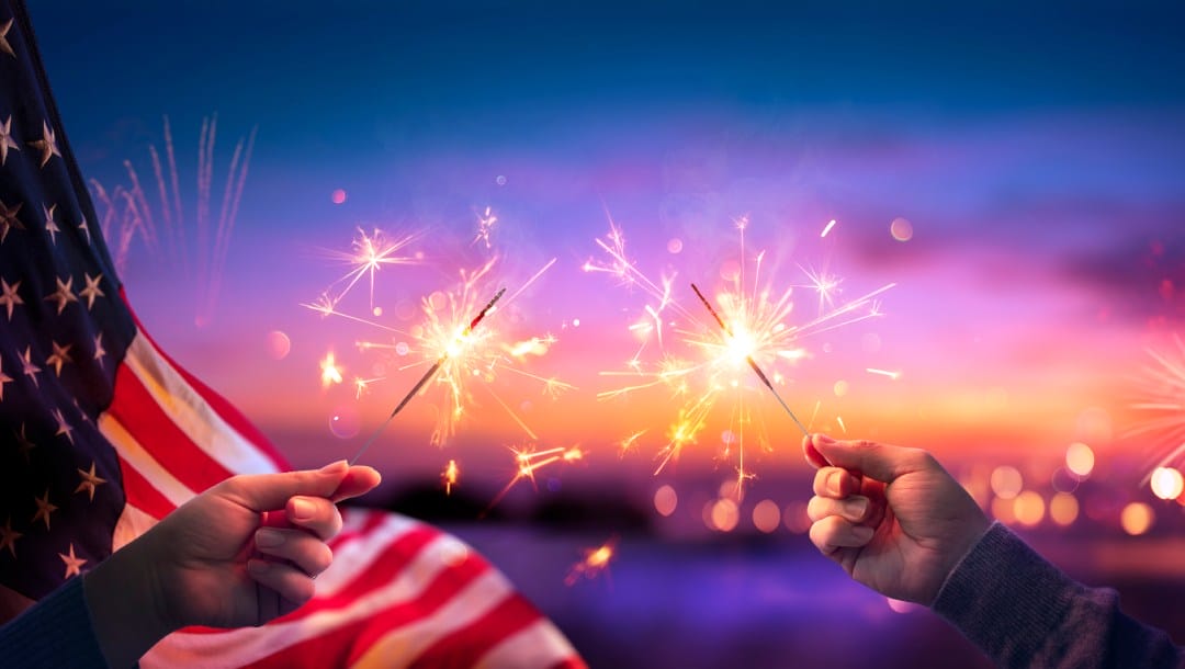 Hands holding sparklers in front of an American flag.