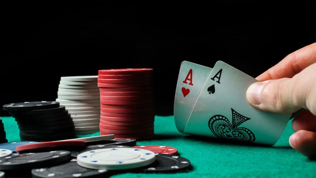 Hand displaying cards at a poker table, revealing an Ace of Hearts and an Ace of Spades, surrounded by poker chips.