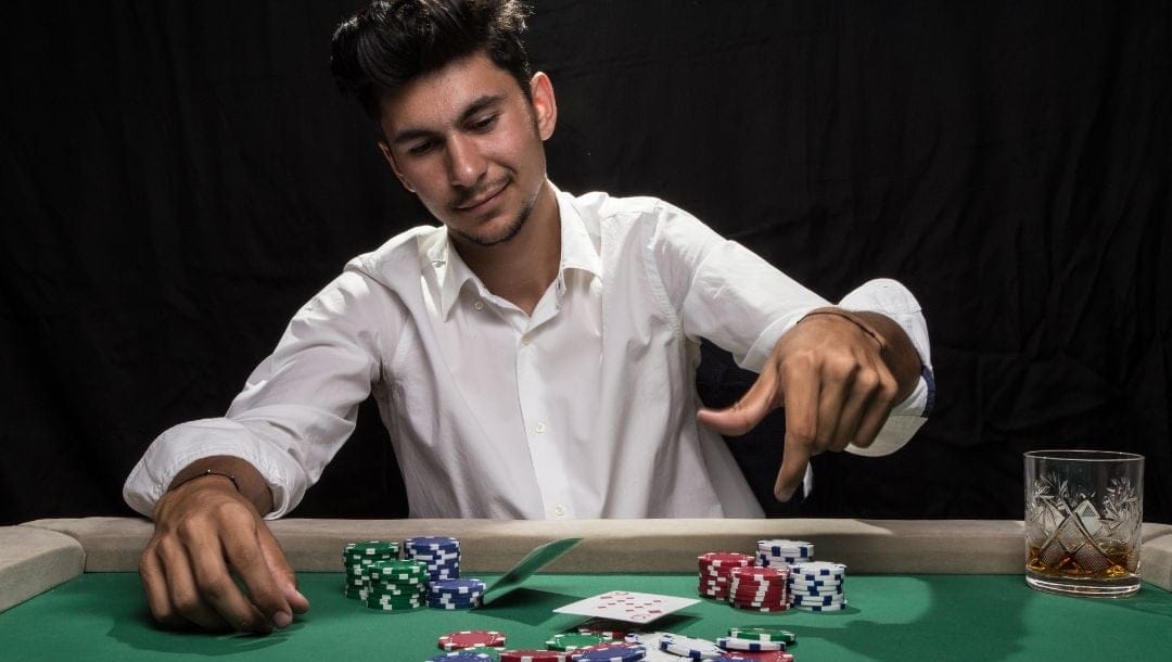 A man in action at a poker table, tossing playing cards down, with casino chips neatly arranged in front of him.
