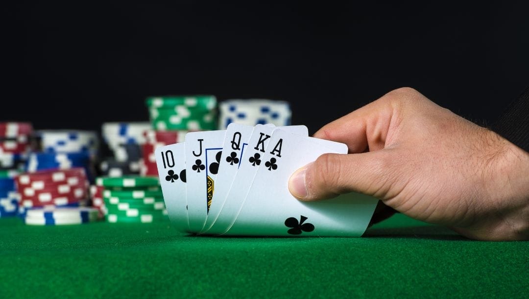 A hand holding Royal Flush in poker and poker chips chips arranged on a poker table.